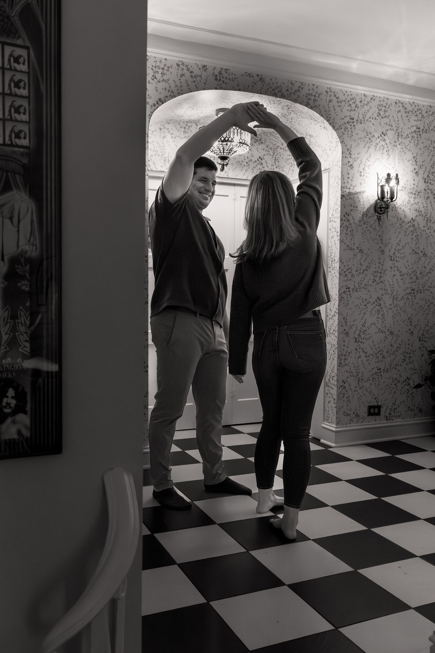 Two people walk down a hallway with black and white checkered floor tiles in a black and white photograph.