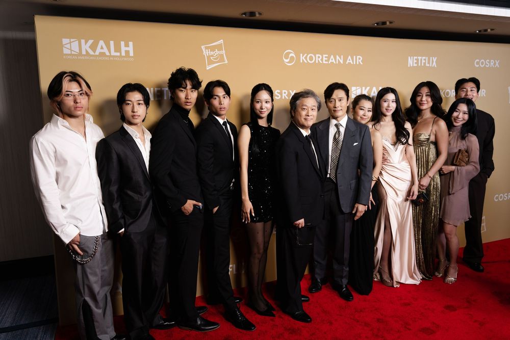 Group of elegantly dressed people posing on a gold carpet at a Korean Air and Netflix event.