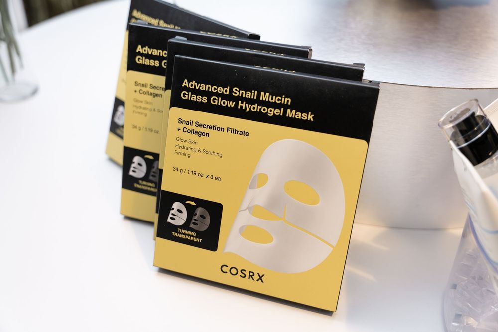 COSRX Advanced Snail Mucin Glass Glow Hydrogel Face Masks stacked in yellow and black packaging boxes.