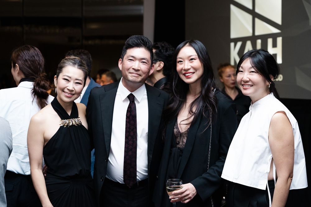 Four people in black attire smiling together at a formal event near a KAH branded backdrop.