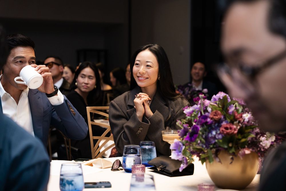 People seated at a table during a formal event, smiling and engaged in conversation with floral centerpieces.
