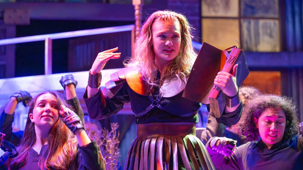 A group of performers in colorful costumes stand together on stage during a theatrical production.