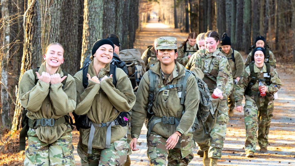 Military personnel in camouflage uniforms stand in formation while performing a group exercise outdoors.