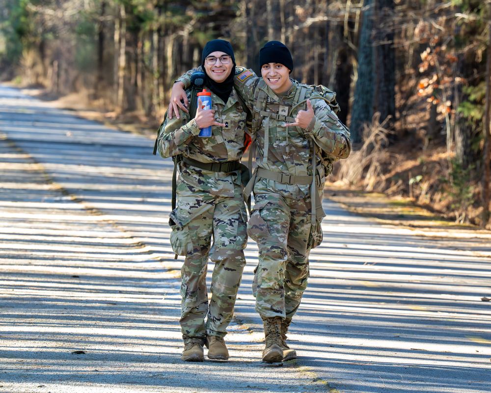 Military personnel walk along a snowy path during winter training exercises in woodland terrain.