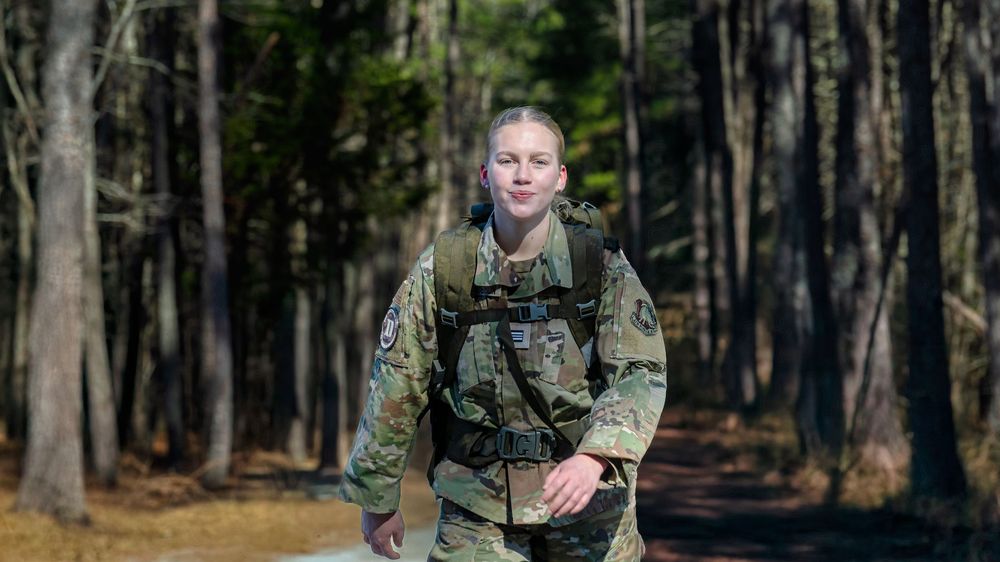 Military personnel in camouflage uniforms stand in formation during a training exercise in a wooded area.