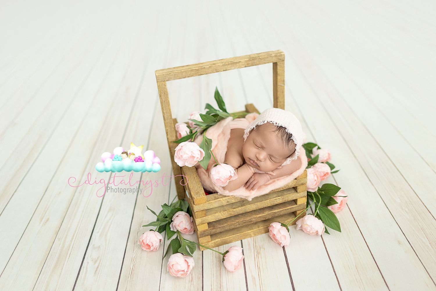 A sleeping newborn baby rests peacefully in a wooden frame prop with pink roses on a white wooden floor.