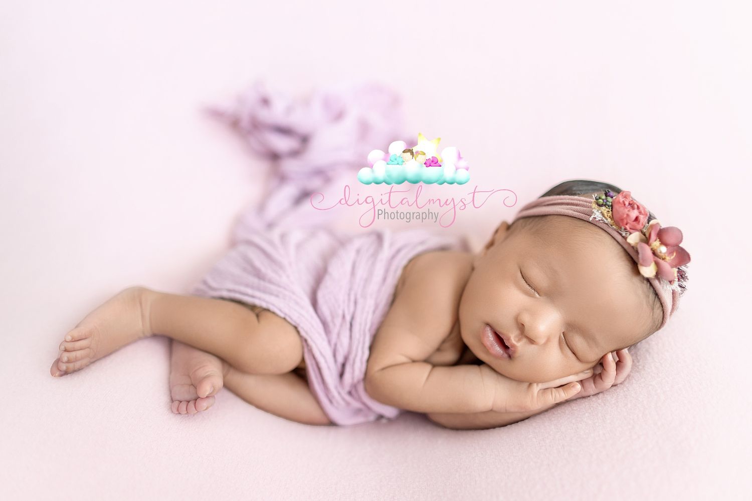A sleeping newborn baby wearing a lavender romper lies peacefully on a soft blanket in a side pose.