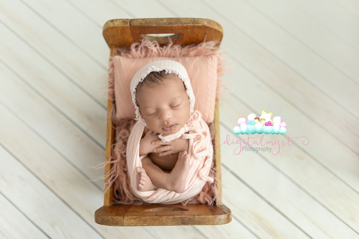 A sleeping newborn baby wearing pink is photographed on a white wooden floor with delicate floral decorations.