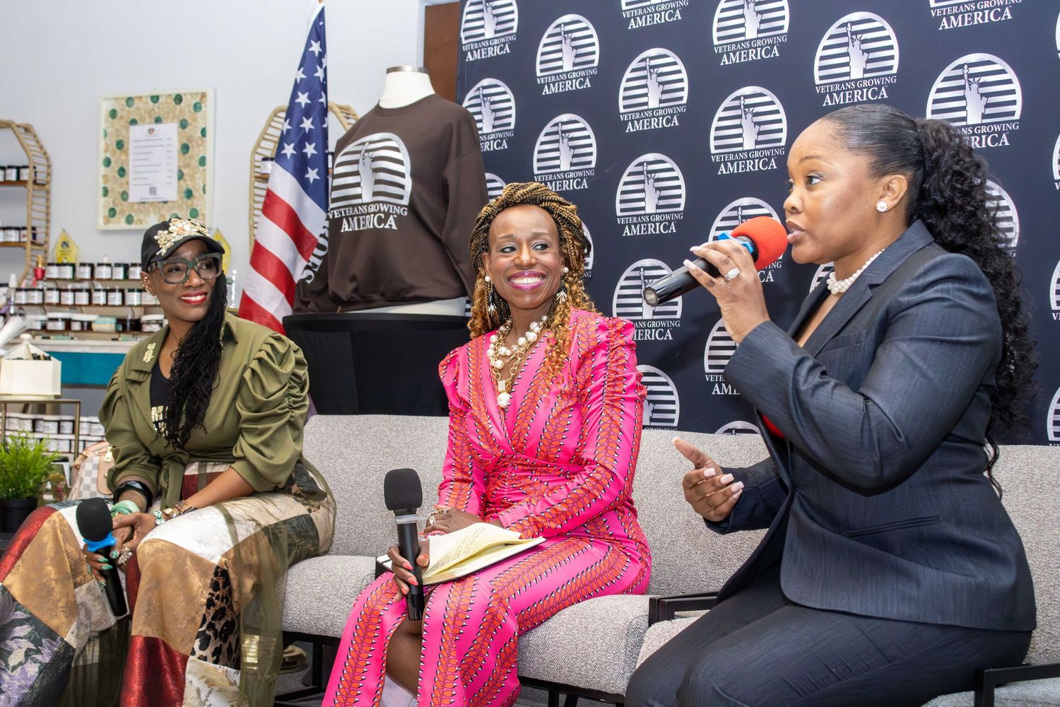 Three women engaged in a panel discussion at a professional event, with an American flag visible in the background.