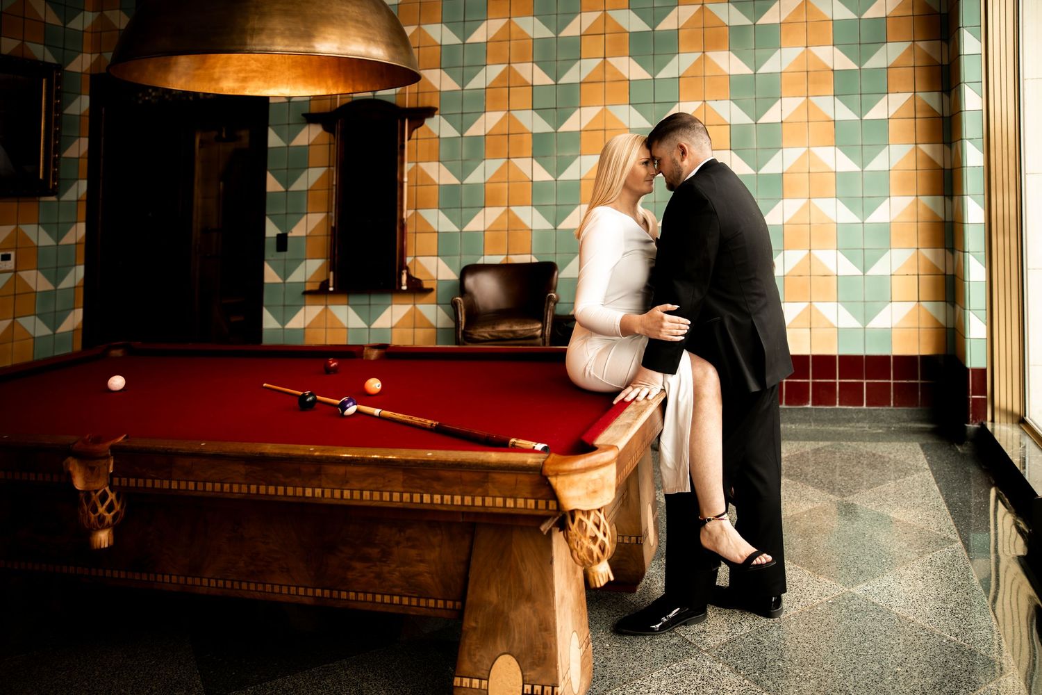 Couple having engagement photos at Bottleworks Hotel, girl sitting on pool table, Indianapolis engagement session.