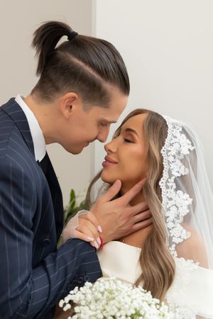 Bride and groom share an intimate moment, touching foreheads, as she holds baby's breath flowers in a white veil.