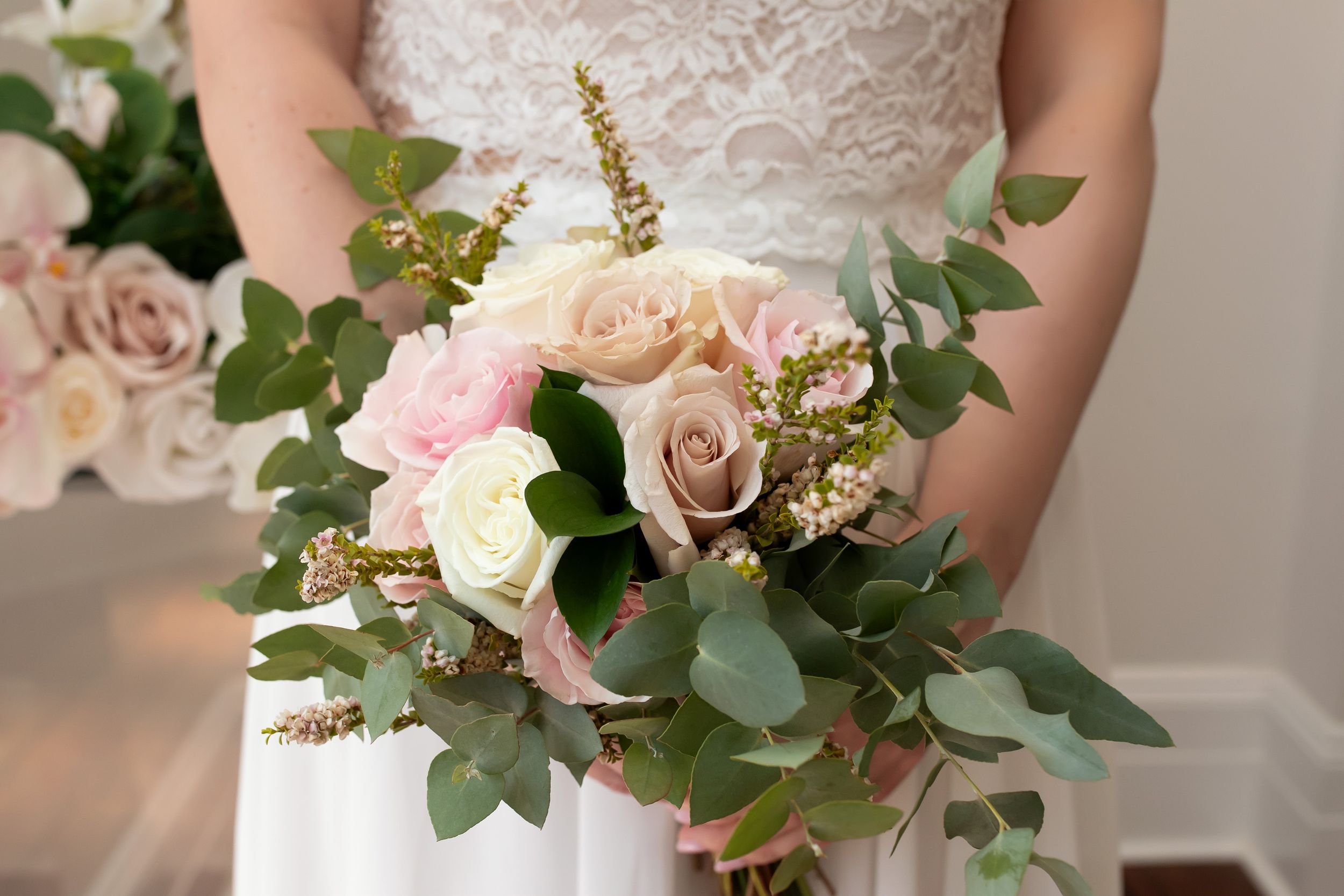 Bride holds a lush bouquet of blush and cream roses with eucalyptus greenery on her wedding day.