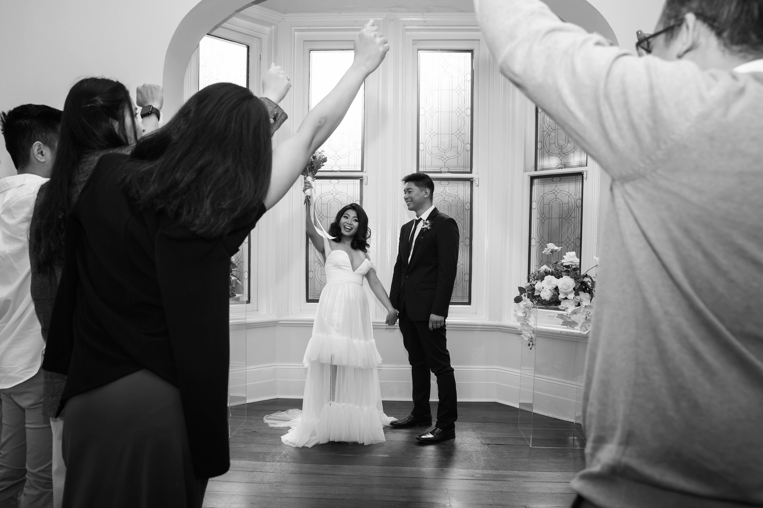 Black and white photo of bride and groom entering wedding reception under arch of raised hands.