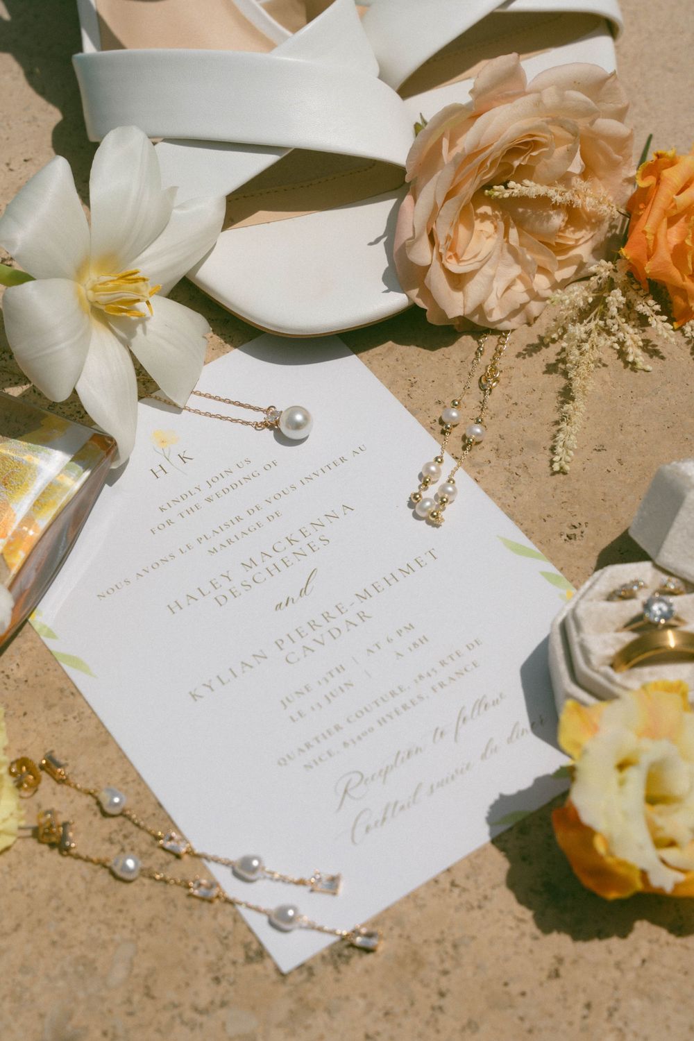 Elegant white wedding invitation cards displayed with fresh flowers and pearls on a textured beige surface.
