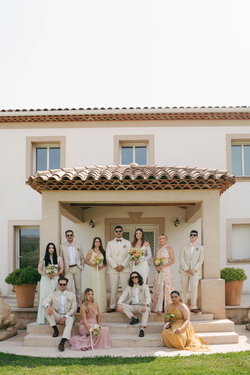 Wedding party in neutral colors poses on Mediterranean style patio with white stucco walls and terracotta roof tiles.