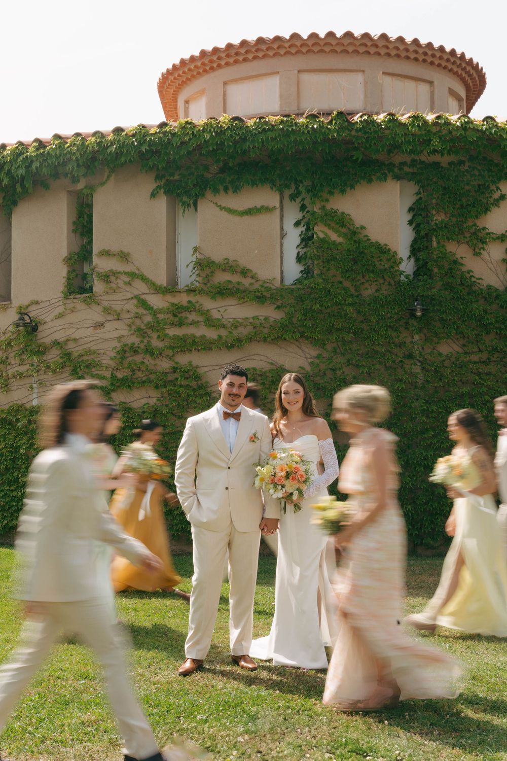 Wedding party in light colored attire walks and poses in motion blur effect against an ivy-covered wall.