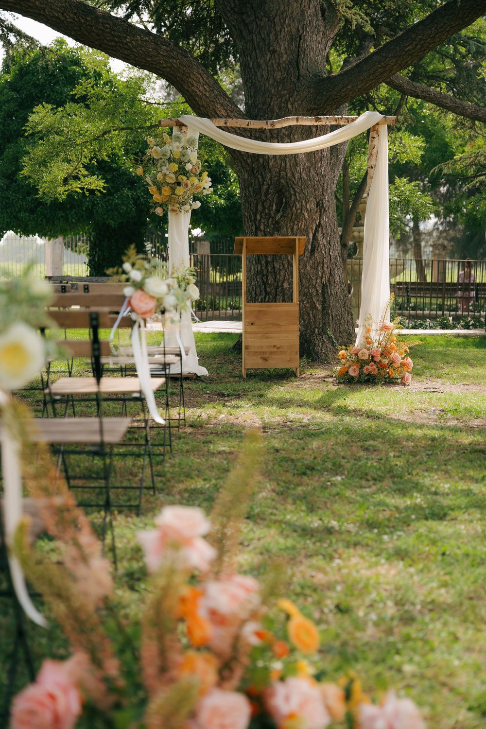 Installation de lieu de mariage en plein air rustique avec du tissu blanc drapé entre les arbres et des arrangements floraux éparpillés dans