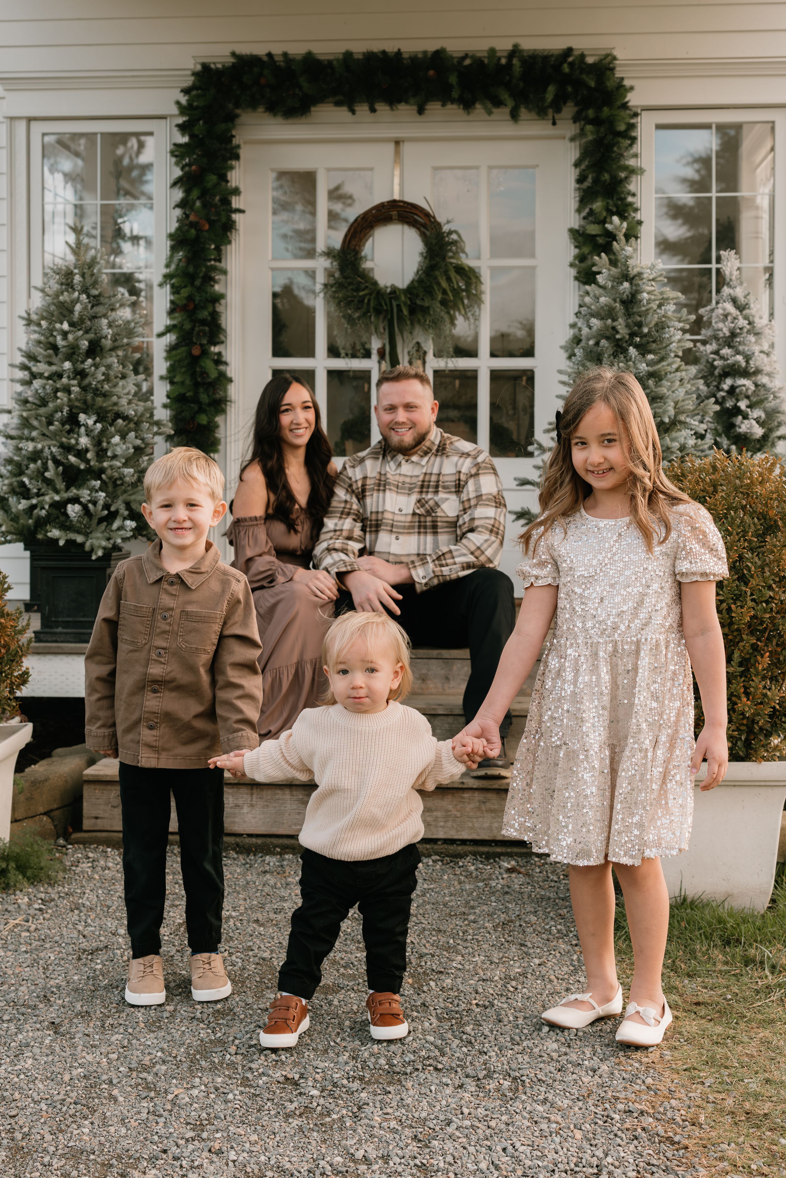 A family poses together on their front porch decorated with Christmas greenery and a wreath during the holiday season.
