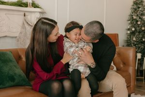A family shares a tender moment together on a brown leather couch with a Christmas tree visible in the background.