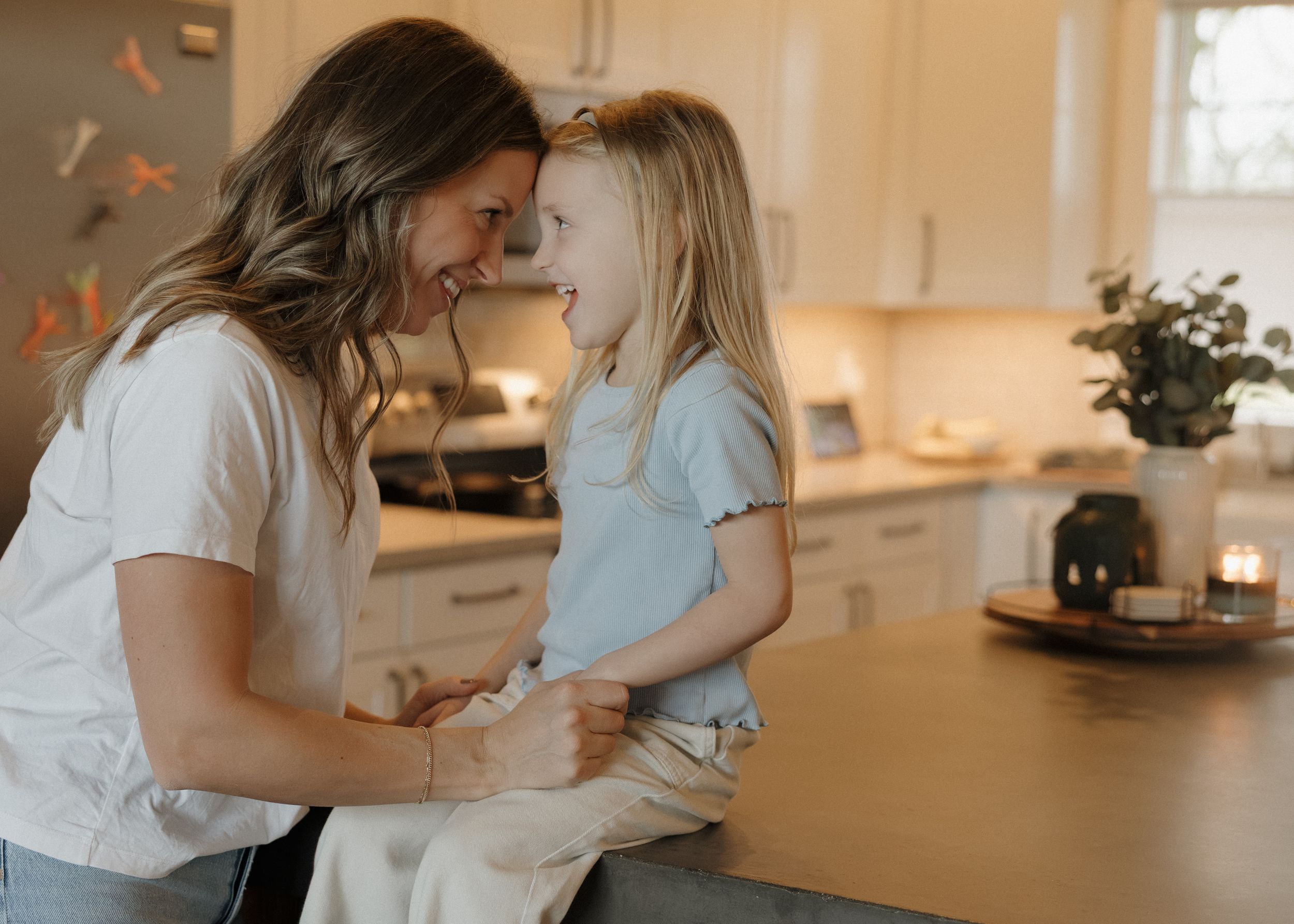 A tender moment shared between parent and child in a bright modern kitchen with warm lighting and floating butterflies.