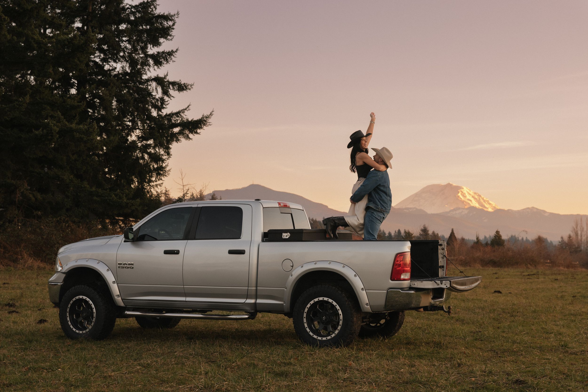 Scenic mountain landscape at sunset with pickup trucks parked on grassy hilltop overlook.