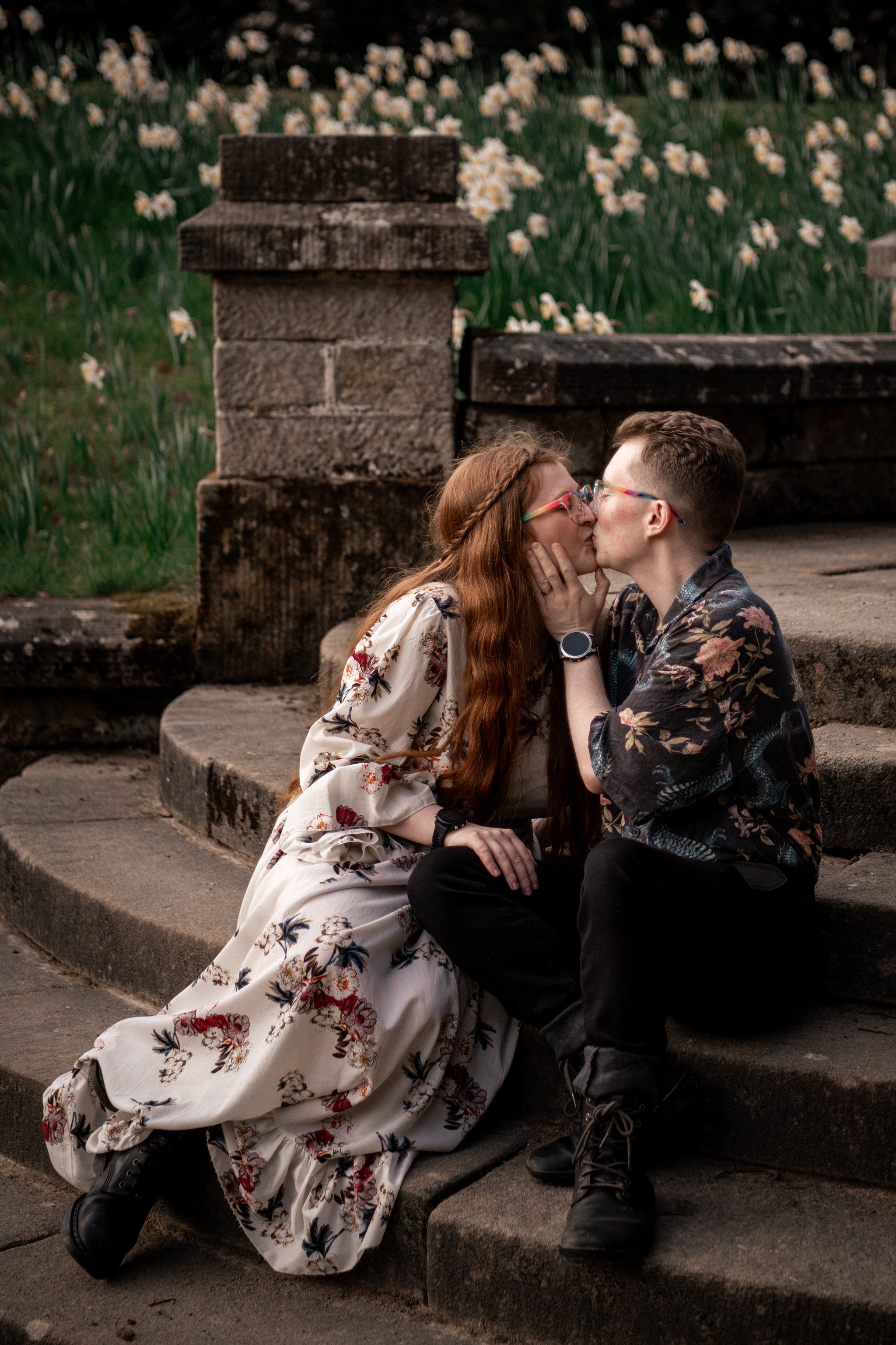 A romantic couple shares intimate moments on stone steps in a garden setting wearing black and floral attire.