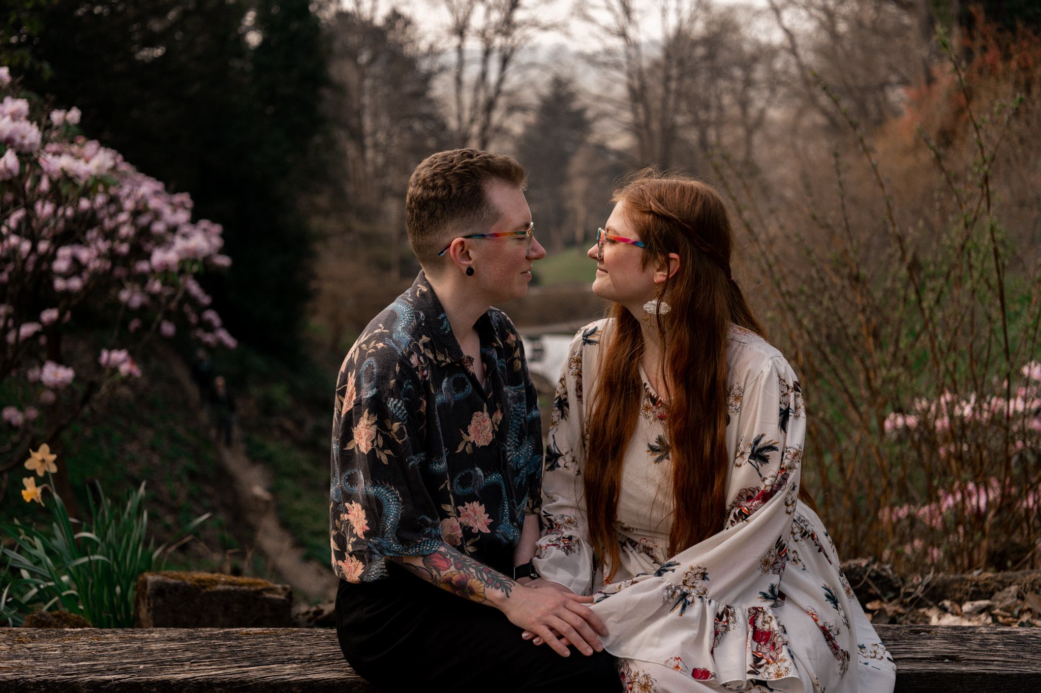 Two people share an intimate moment on stone steps amidst flowering trees in a park garden.