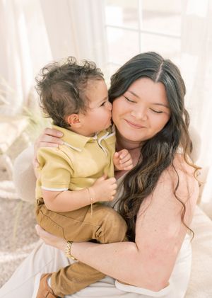 A tender moment between parent and toddler in yellow polo shirt as they share an intimate embrace in soft natural light.