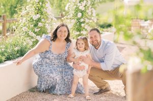 A family sits together on a garden bench surrounded by blooming white flowers on a sunny spring day.