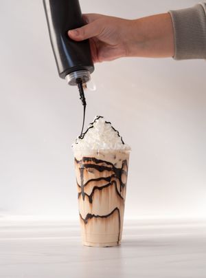 Chocolate sauce being drizzled over a whipped cream topped frozen coffee drink.
