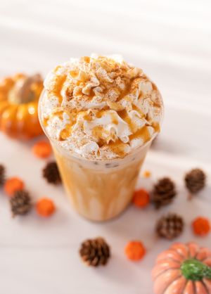 A pumpkin spice latte topped with whipped cream and caramel surrounded by fall decorations.