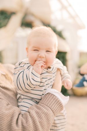 A baby wearing a striped shirt and gray sweater smiles while playing in a bright, cozy indoor setting.