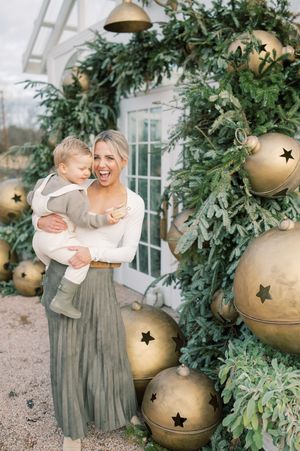 A festive holiday scene with large gold ornaments and greenery decorations against a light-colored wall.