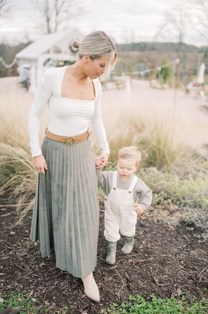 A parent and small child walk together through tall grass and mulch in coordinating white and gray outfits.