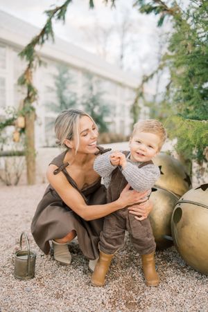A heartwarming moment captured in a greenhouse setting with decorative vintage planters and evergreen foliage.