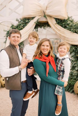 A family poses together in front of a holiday archway decorated with greenery and cream-colored fabric.