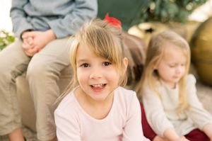 A happy child wearing a pink dress and gray sweater plays energetically on a light-colored carpet.