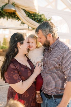 A happy family shares an intimate moment together outdoors with greenery and soft lighting in the background.