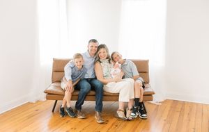 Family sitting together on brown couch in bright minimalist room with hardwood floors.