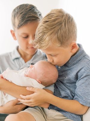 Two young boys tenderly holding and looking down at a newborn baby wrapped in white.