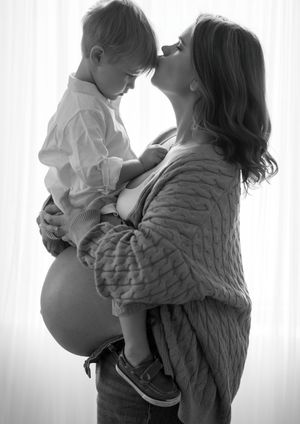A tender black and white portrait of a pregnant woman in a sweater sharing an intimate moment with a small child.