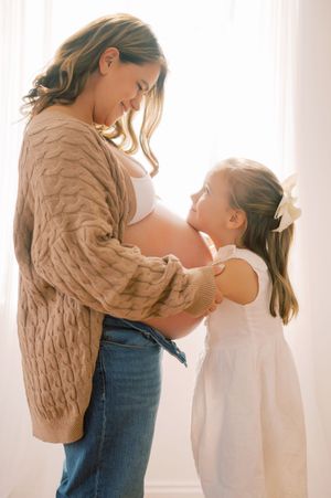 A heartwarming maternity photoshoot featuring a mother and child sharing tender moments against a light background.