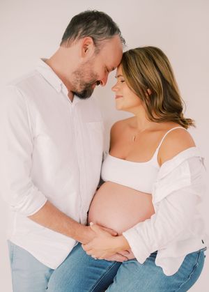 Intimate maternity photo of couple in white shirts against light background.
