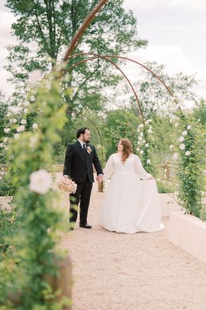 A couple shares a romantic moment on a garden path surrounded by lush greenery and trees on their wedding day.