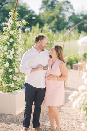 A couple shares tender moments in an outdoor garden setting with white floral arches and gravel paths.