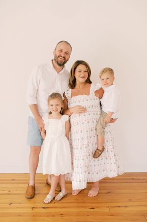 Family portrait against white wall with wooden floor.