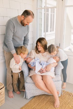 Family gathers together on a gray armchair in a bright sunlit room with white walls and natural decor.