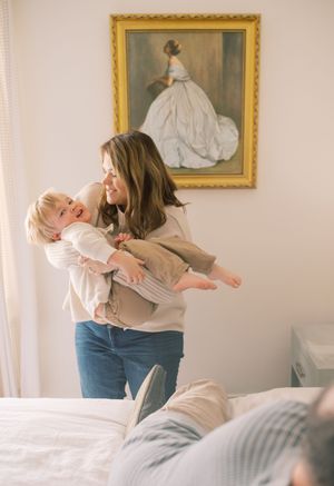 A joyful moment shared in a bedroom with a framed painting of a woman in a white dress hanging on the wall behind.
