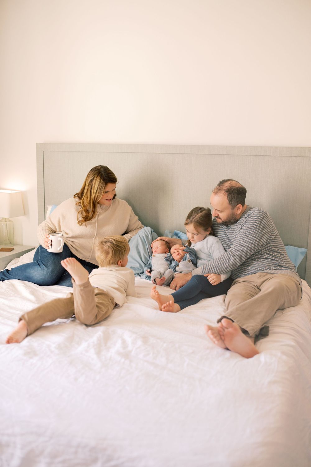 Family relaxing together on white bed with children and baby in casual clothing at home.