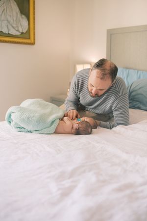 A tender moment between an adult and baby lying together on a white bed with a mint green blanket.